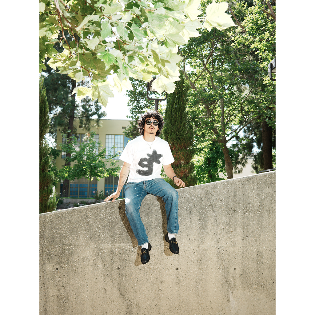 Person sitting on a concrete ledge with trees in the background wearing g & star white t-shirt