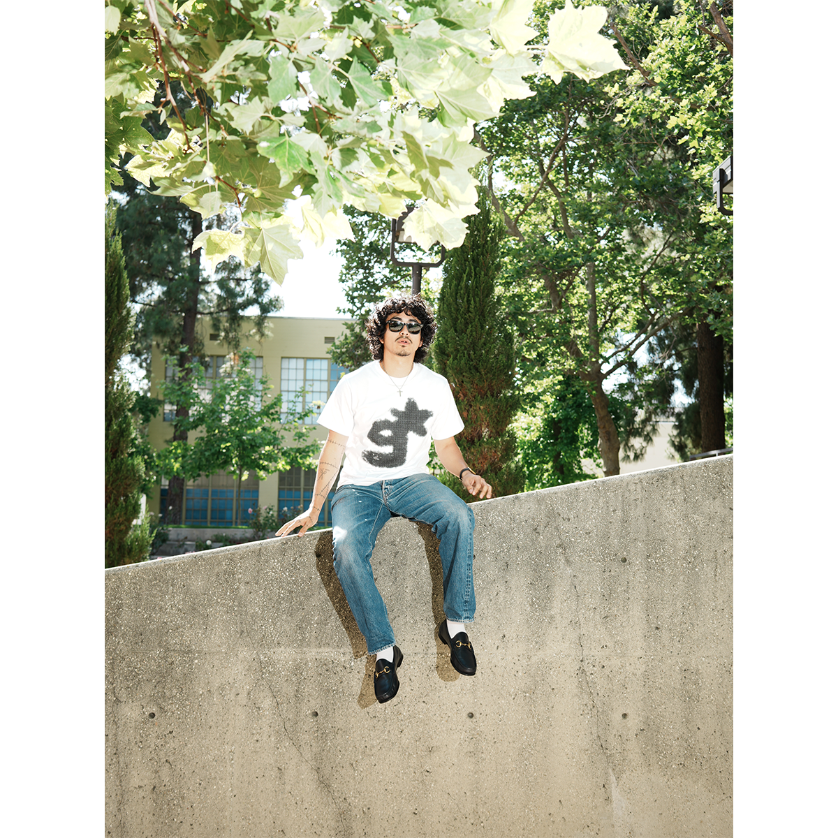 Person sitting on a concrete ledge with trees in the background wearing g & star white t-shirt