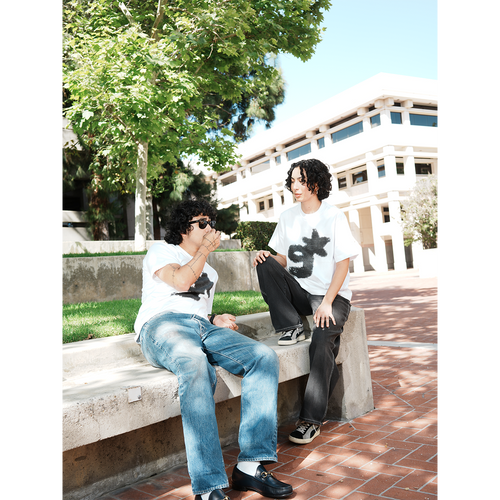 Two people sitting on a concrete bench outdoors with trees and a building in the background wearing g & star white t-shirt