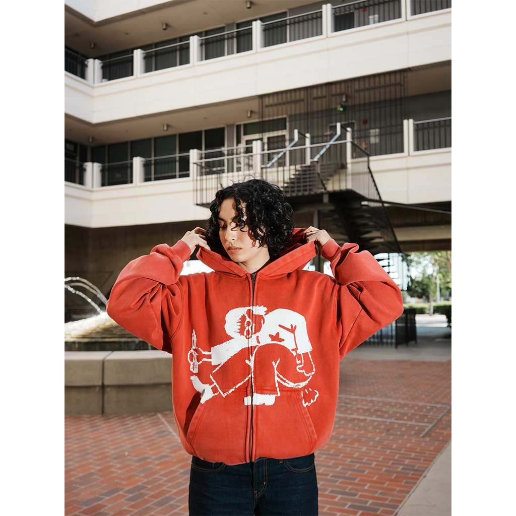 Model wearing a red hoodie with a graphic design in an outdoor setting