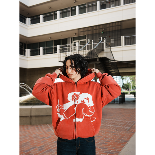 Model wearing a red hoodie with a graphic design in an outdoor setting
