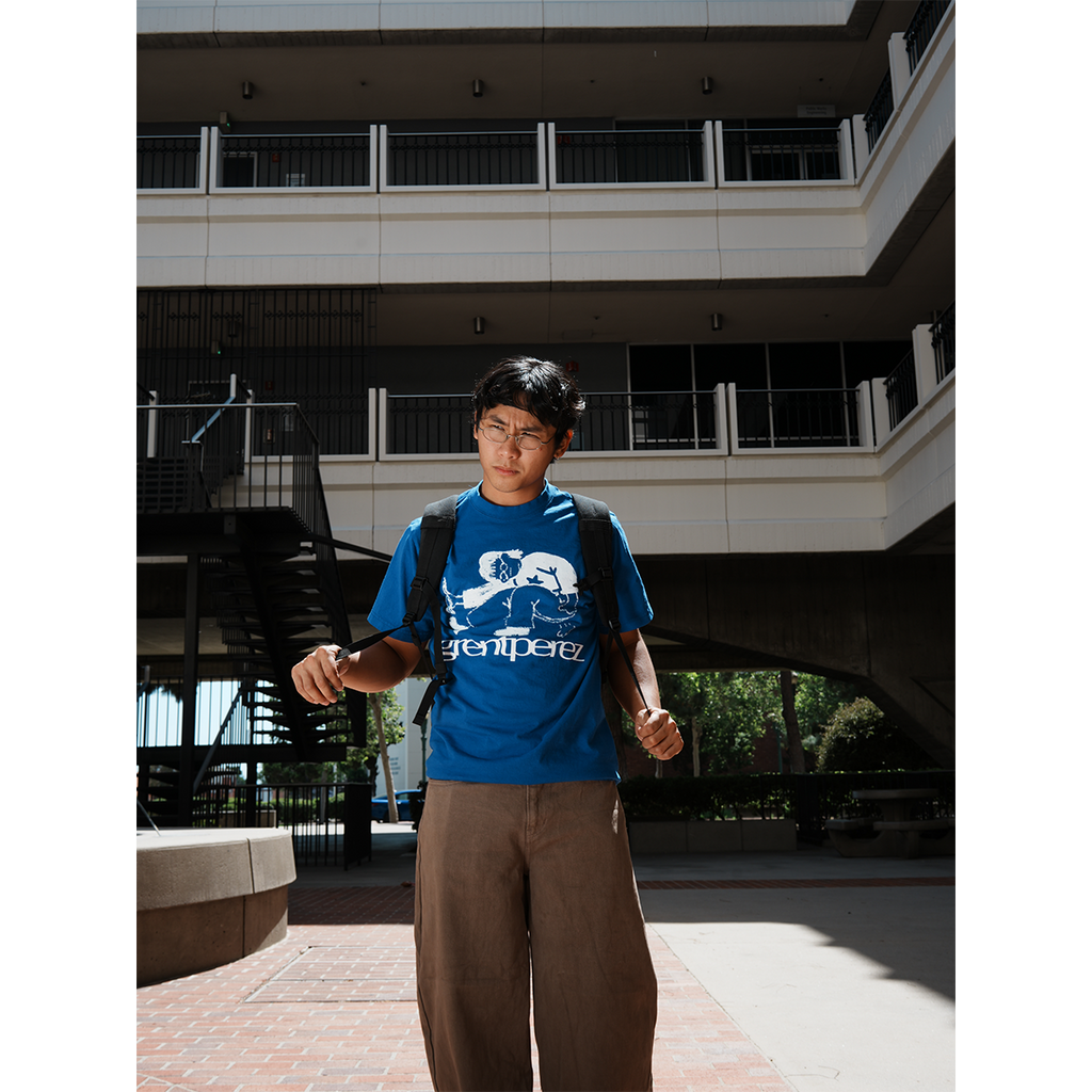 grentperez wearing a blue t-shirt with a logo and text, standing in front of a building.