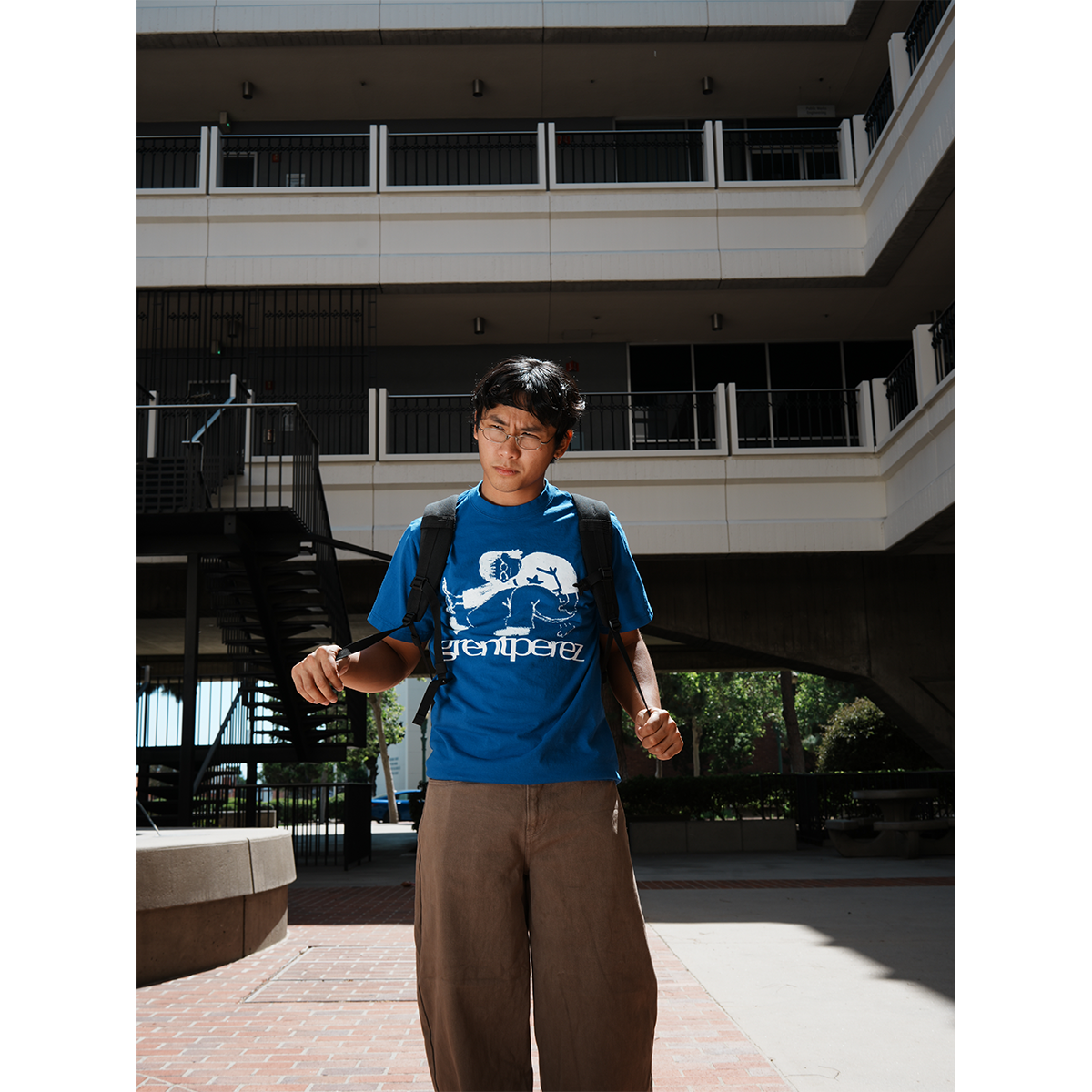 grentperez wearing a blue t-shirt with a logo and text, standing in front of a building.